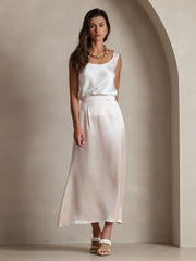 Woman wearing a sleeveless U-neck 19Momme mulberry silk tank top in white with a matching silk skirt.