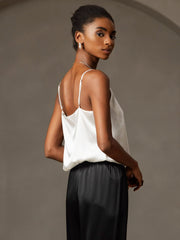 Woman wearing a white 19Momme mulberry silk spaghetti strap camisole with a round neck and black silk pants.