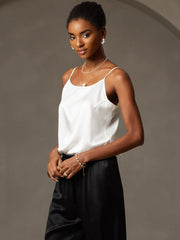 Woman in a white mulberry silk spaghetti strap camisole and black satin pants, adorned with pearl jewelry.