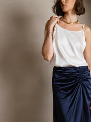 White mulberry silk spaghetti strap camisole with a round neck, paired with a navy ruched skirt.